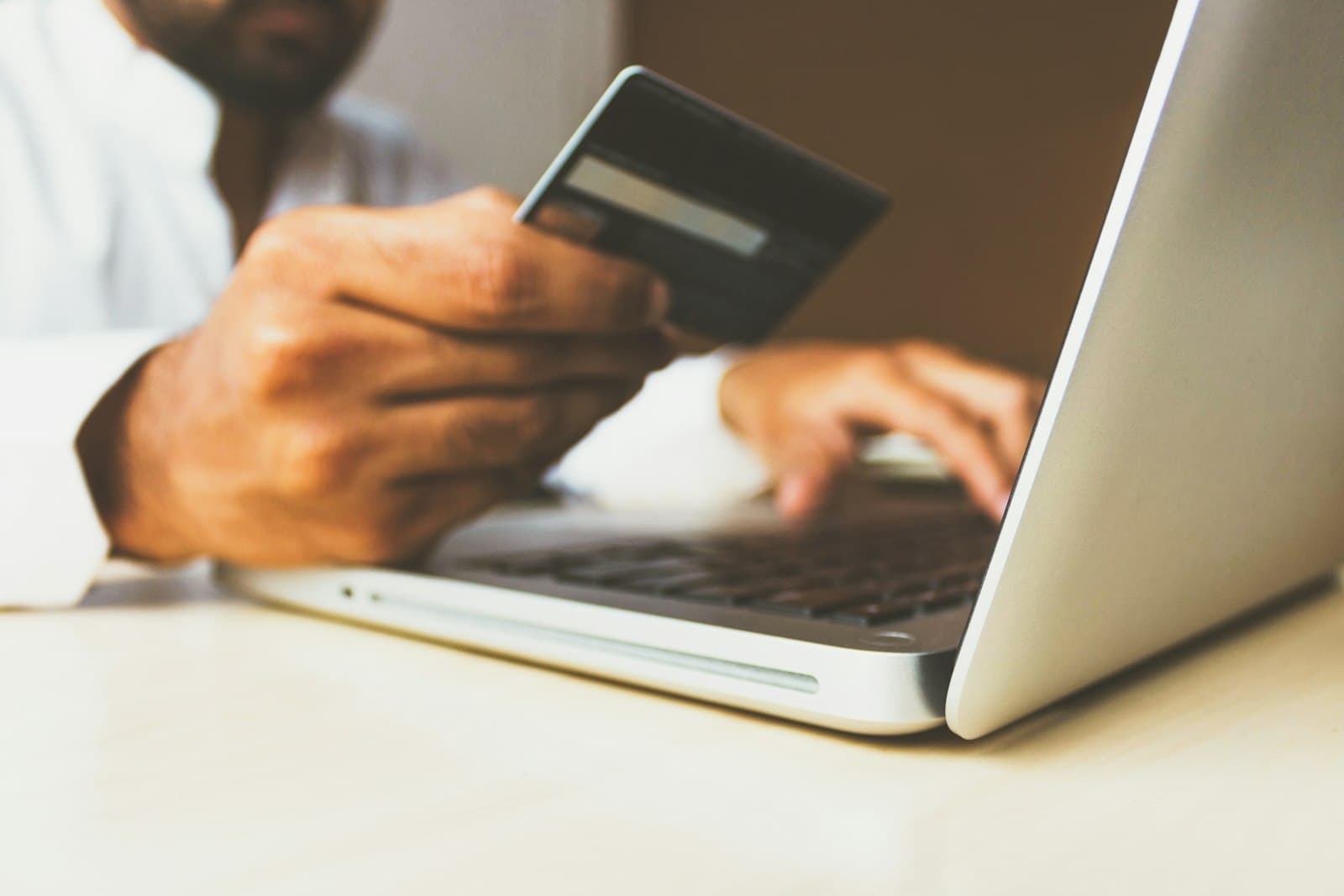 Hands holding a bank card beside an open laptop.
