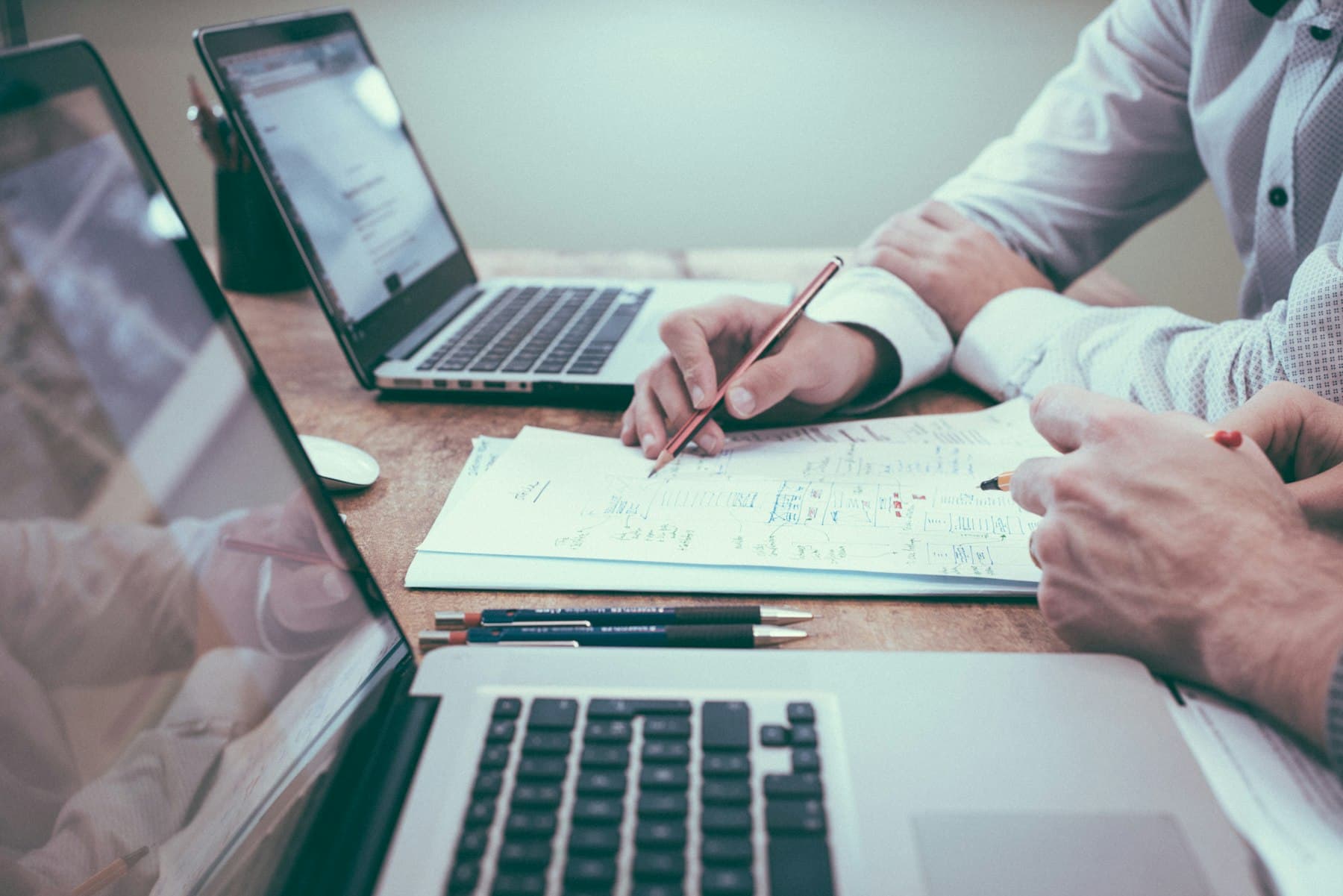 Two people marking a plan on paper between open laptops.