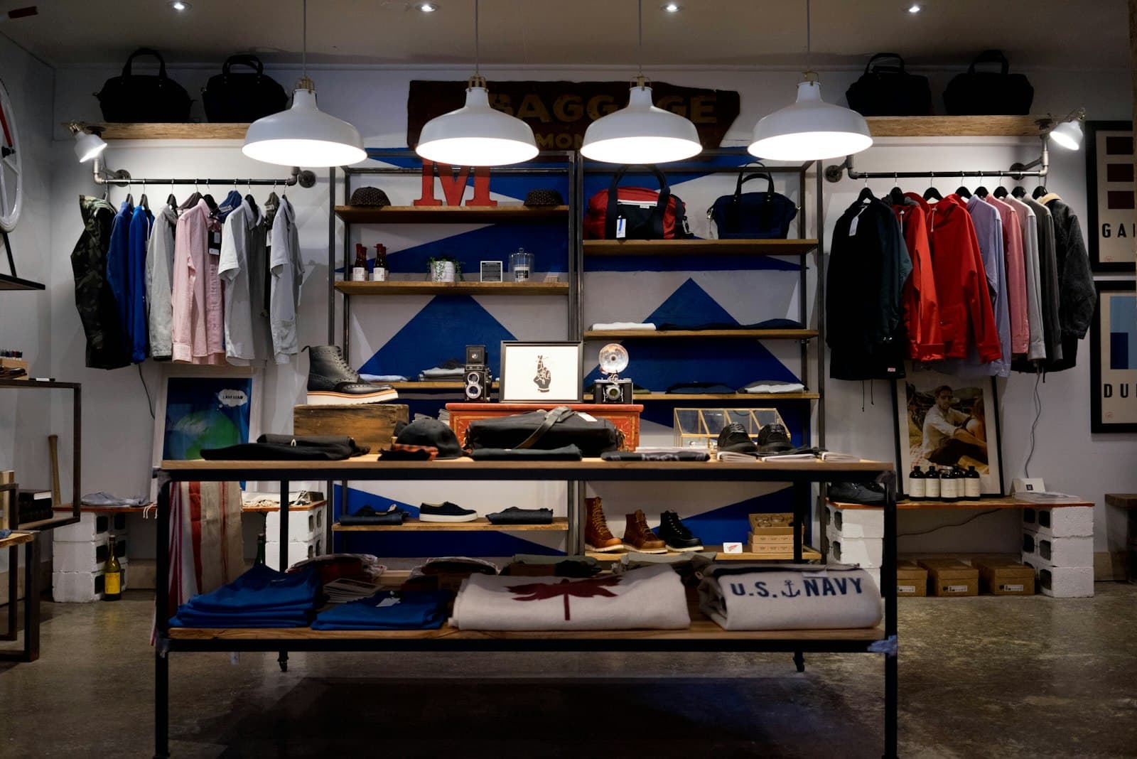 A clothing shop with racks, folded shirts, shelves, and white pendant lights.